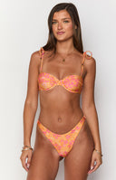 Girl wearing orange bikini top and bottoms with gold jewellery in front of pool chair.